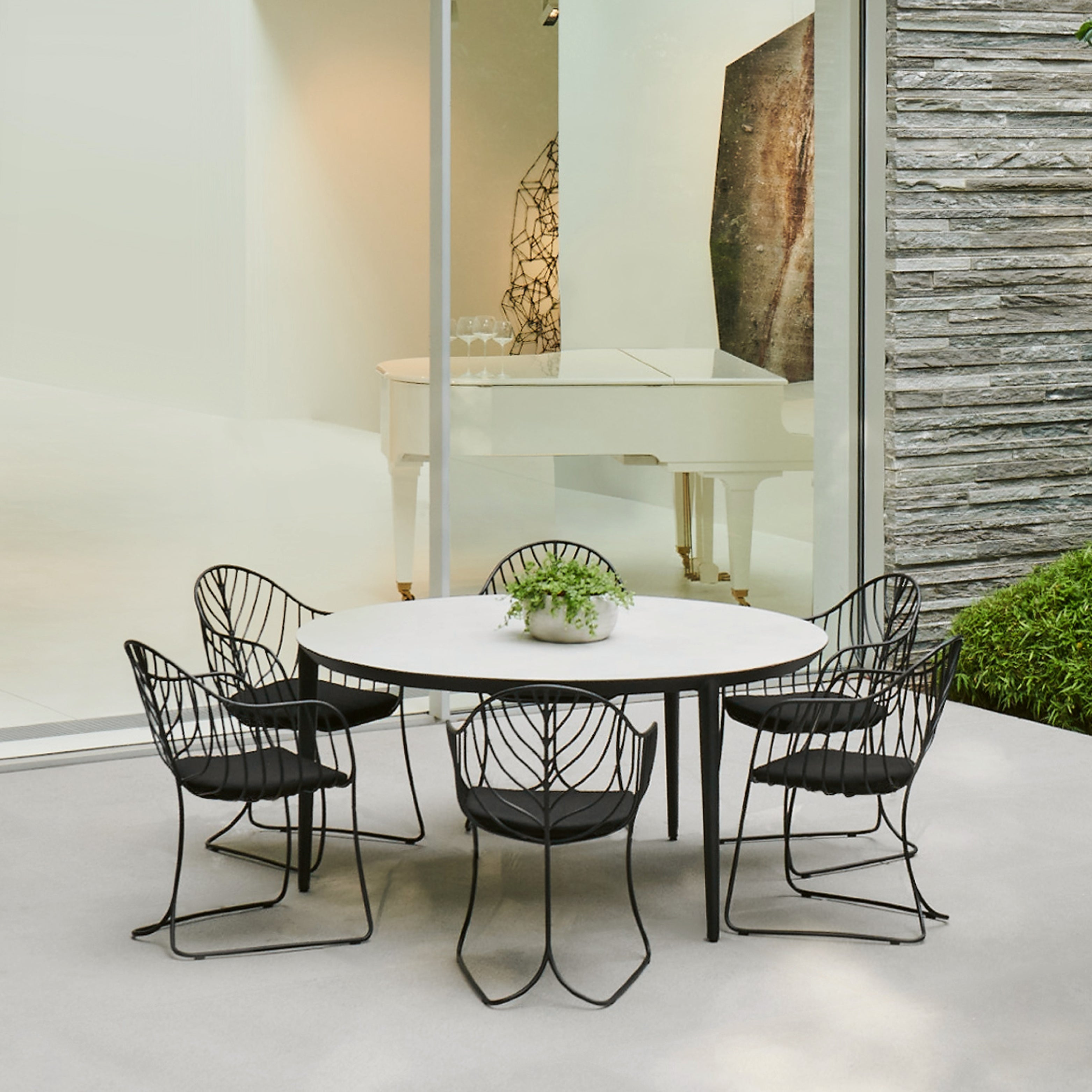 Folia Gartenstühle in schwarzem Metall mit organischem Blattdesign um einen runden Esstisch auf moderner Terrasse – stilvolles Outdoor-Ensemble mit Architekturbezug.