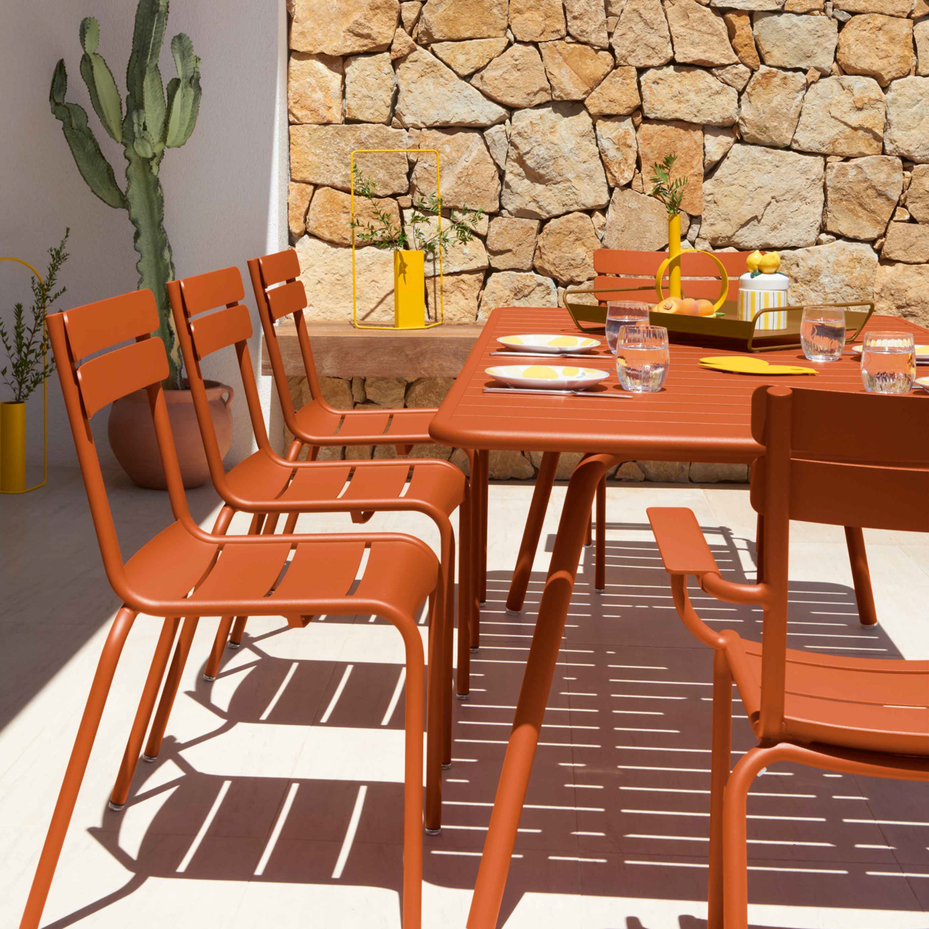 Outdoor-Essgruppe in Terrakotta-Orange – farbenfrohe Gartenmöbel aus Metall im Sommerlicht.