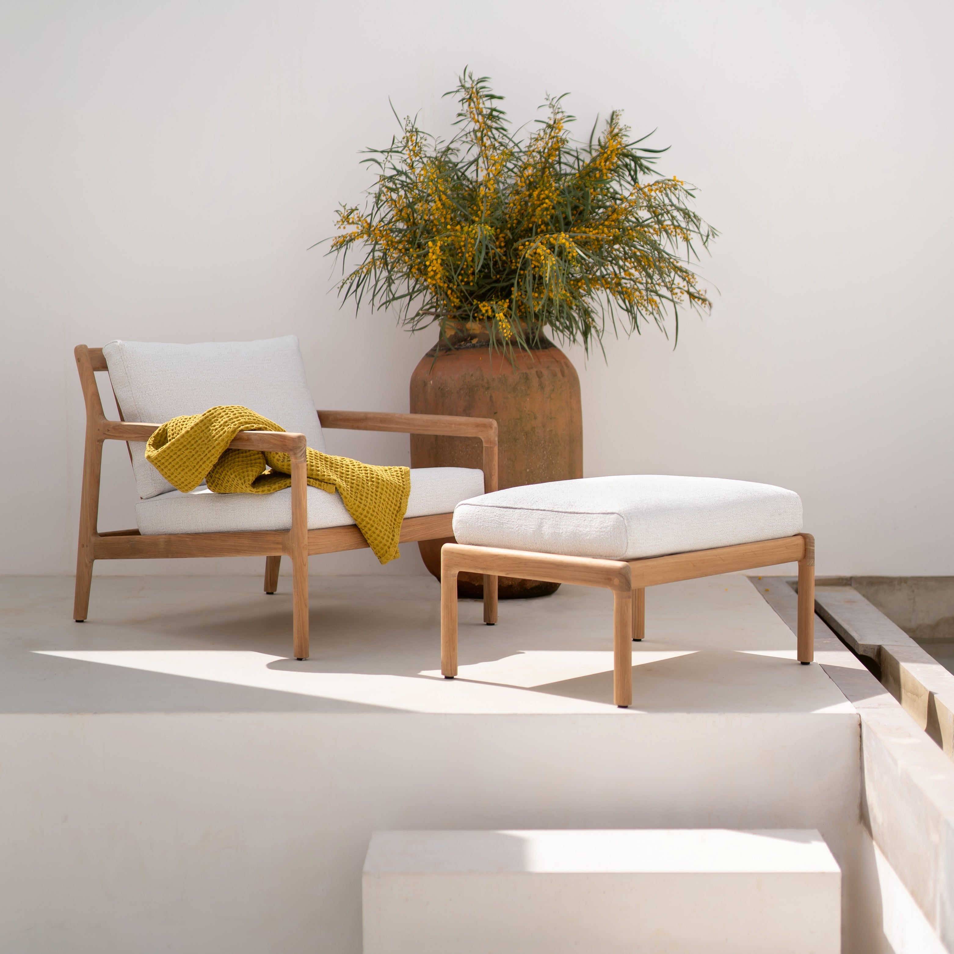 Outdoor-Loungesessel mit Hocker aus Teak und weißen Kissen – stilvoll inszeniert auf heller Terrasse mit Pflanzgefäß.