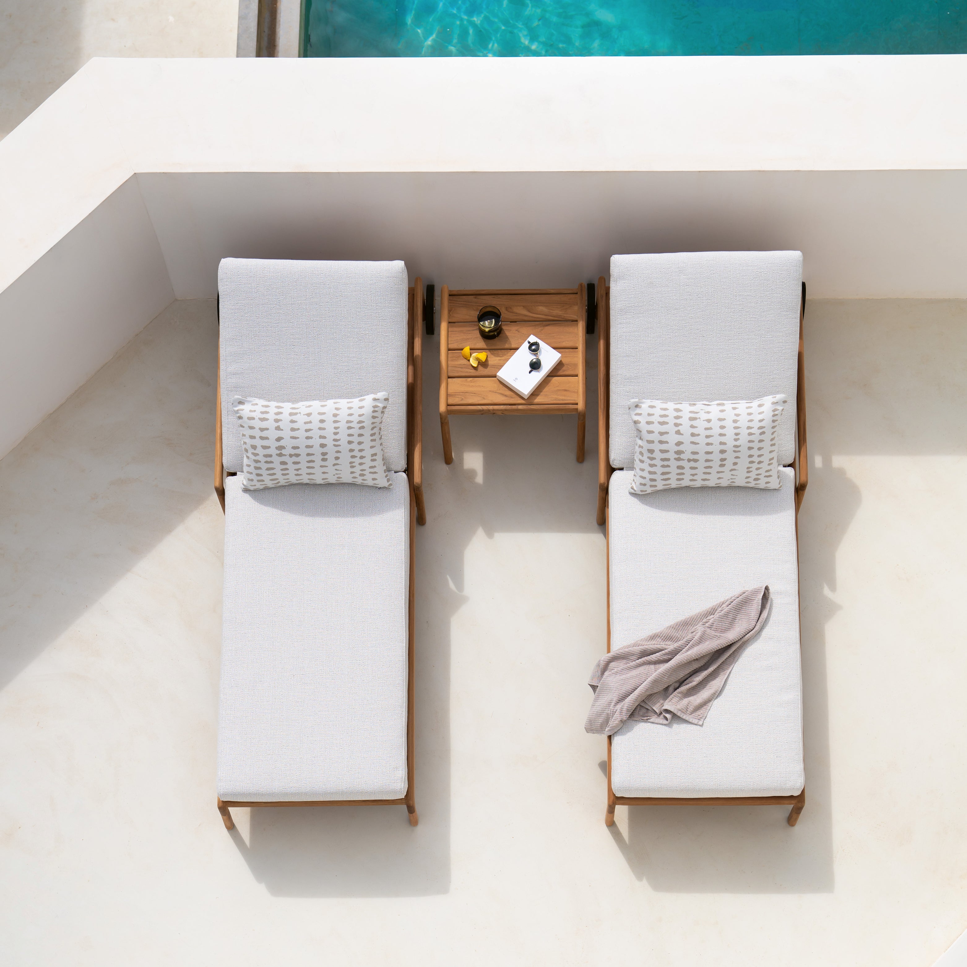 Zwei Sonnenliegen auf Terrasse mit Beistelltisch, helle Stoffe und entspannte Pool-Atmosphäre von oben