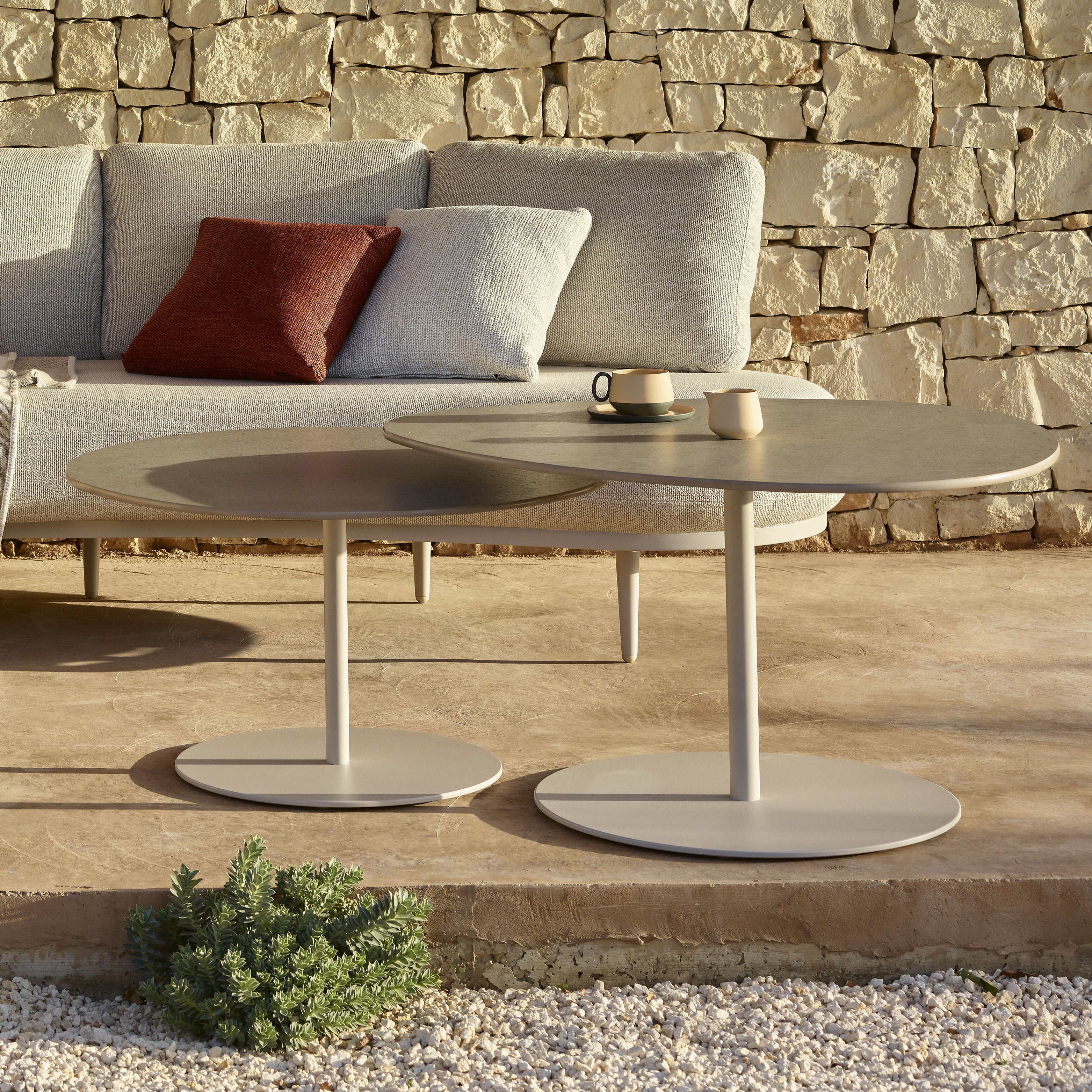 Zwei runde Organix Beistelltische von Royal Botania vor Outdoor-Sofa mit Natursteinwand.