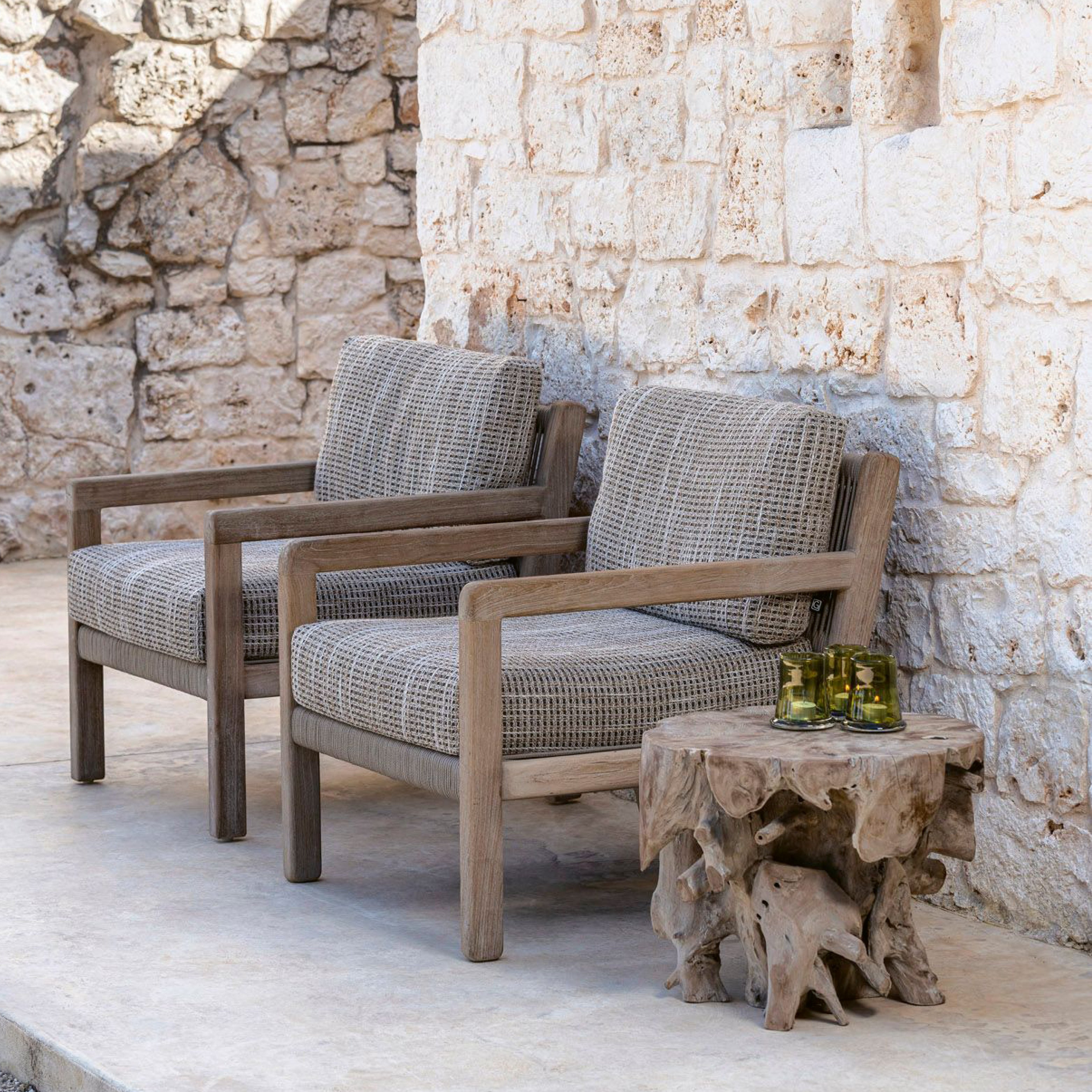 Zwei Outdoor-Sessel von Gommaire mit Teakrahmen und Polsterung – kombiniert mit einem naturgeformten Couchtisch aus Wurzelholz vor Steinwand