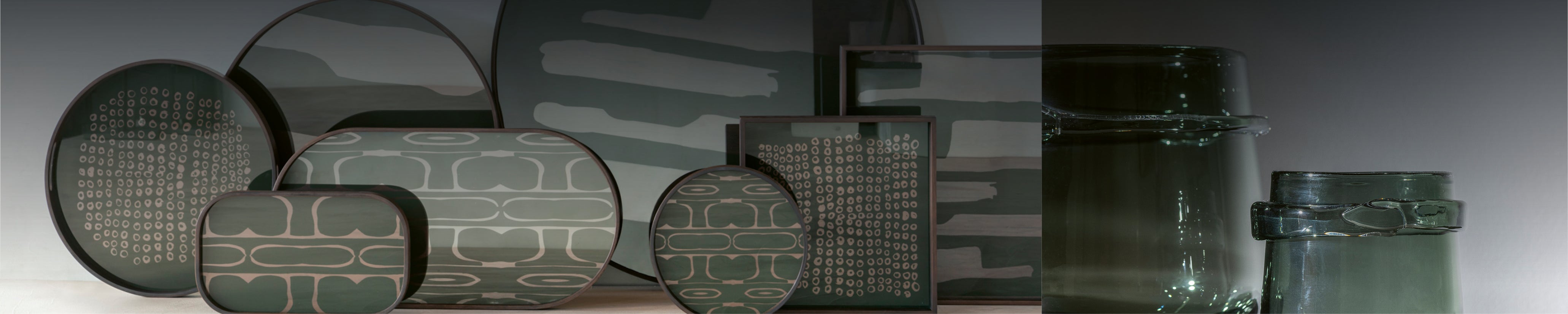 Weitwinkelaufnahme von zwei unterschiedlich großen, mundgeblasenen Scapa Glasvasen in dunklem Grau mit grünlichem Schimmer vor hellem Hintergrund – stilvolle Indoor Accessoires im modernen Ambiente.