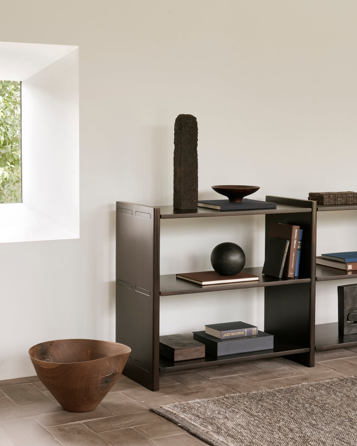 Ethnicraft MORTISE Regal aus Mahagoni in Rose Brown mit Büchern und Dekorationsobjekten in einem Wohnzimmer.