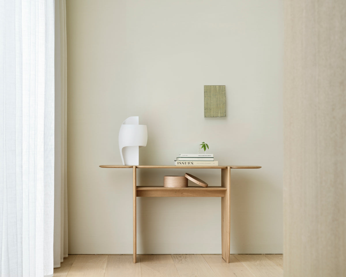 Console PI d'Ethnicraft 130 x 75 cm en chêne, agrémentée d'objets décoratifs, dans une entrée lumineuse.