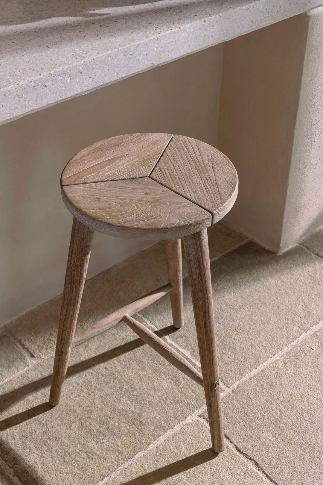 Gros plan sur le tabouret Asti de Gommaire à l'intérieur - en perspective surélevée, en mettant l'accent sur la structure naturelle du teck et les formes claires.
