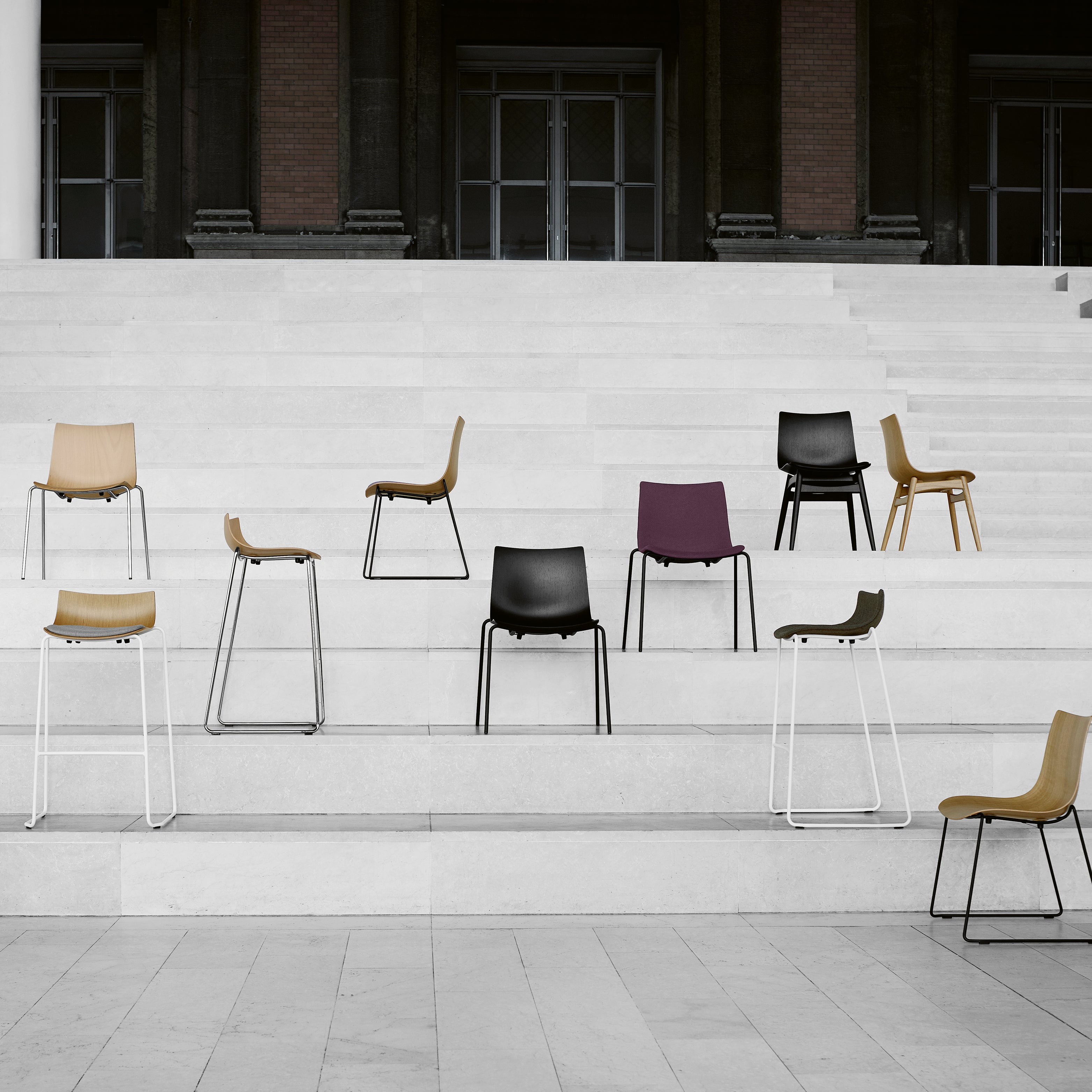 Design-Stühle von Carl Hansen mit Metall- und Holzfüßen auf einer hellen Treppe, minimalistisch und architektonisch inszeniert – Design & Conceptual Kollektion.