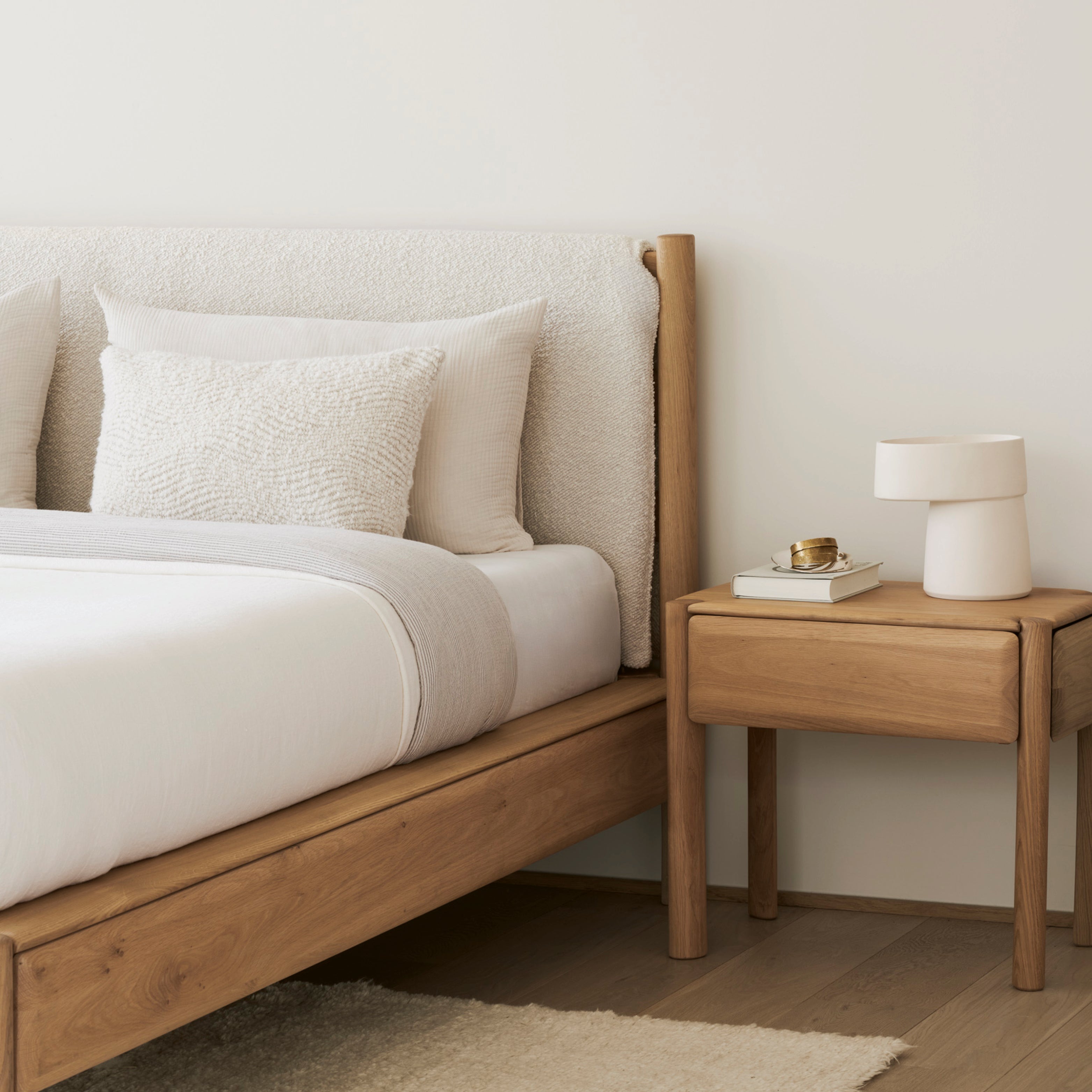 Schlafzimmer mit Massivholzbett, Nachttisch und weichen Textilien in heller, entspannter Atmosphäre