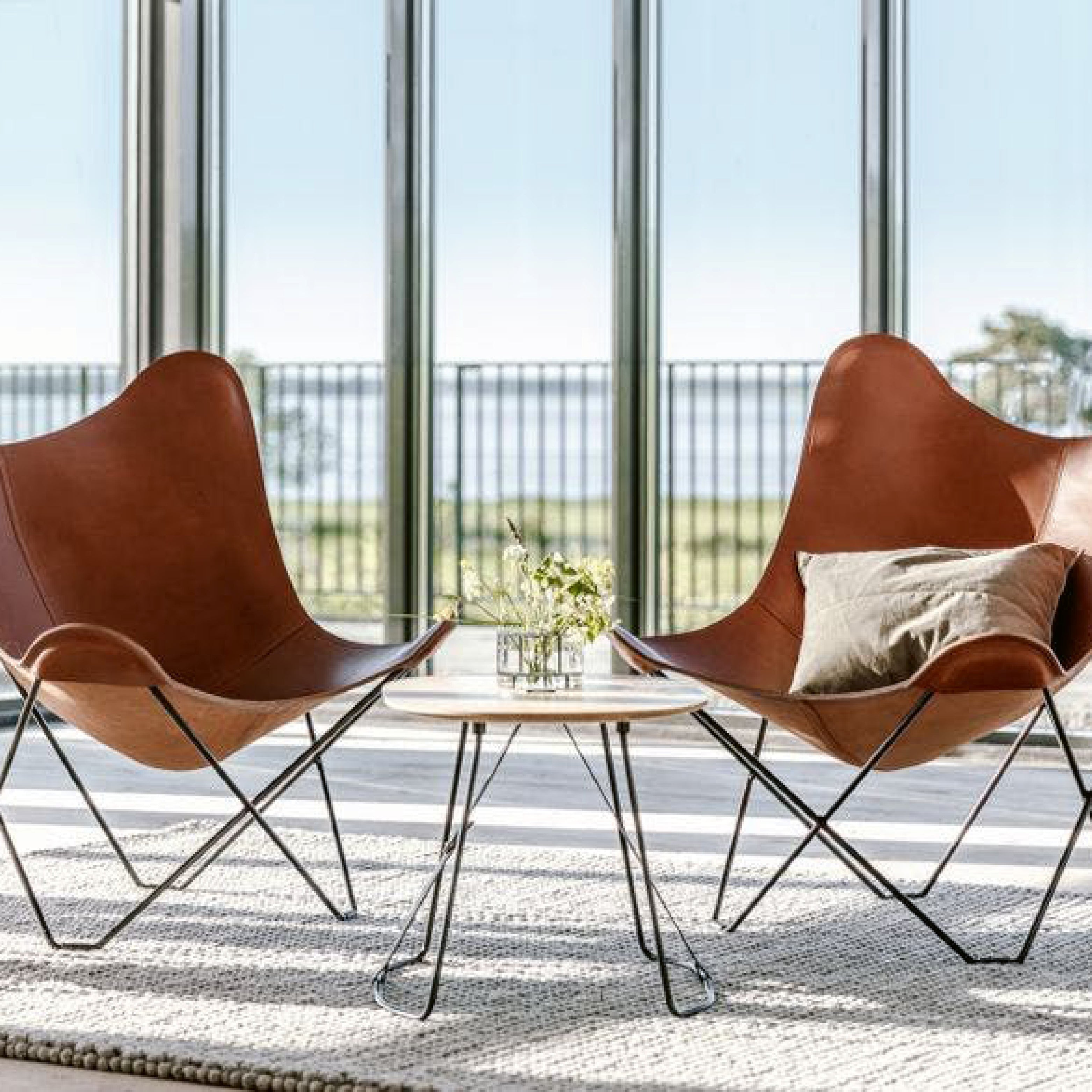 Zwei Butterfly Chairs von Cuero aus braunem Leder – ikonisches Design mit Stahlgestell im lichtdurchfluteten Raum mit Ausblick