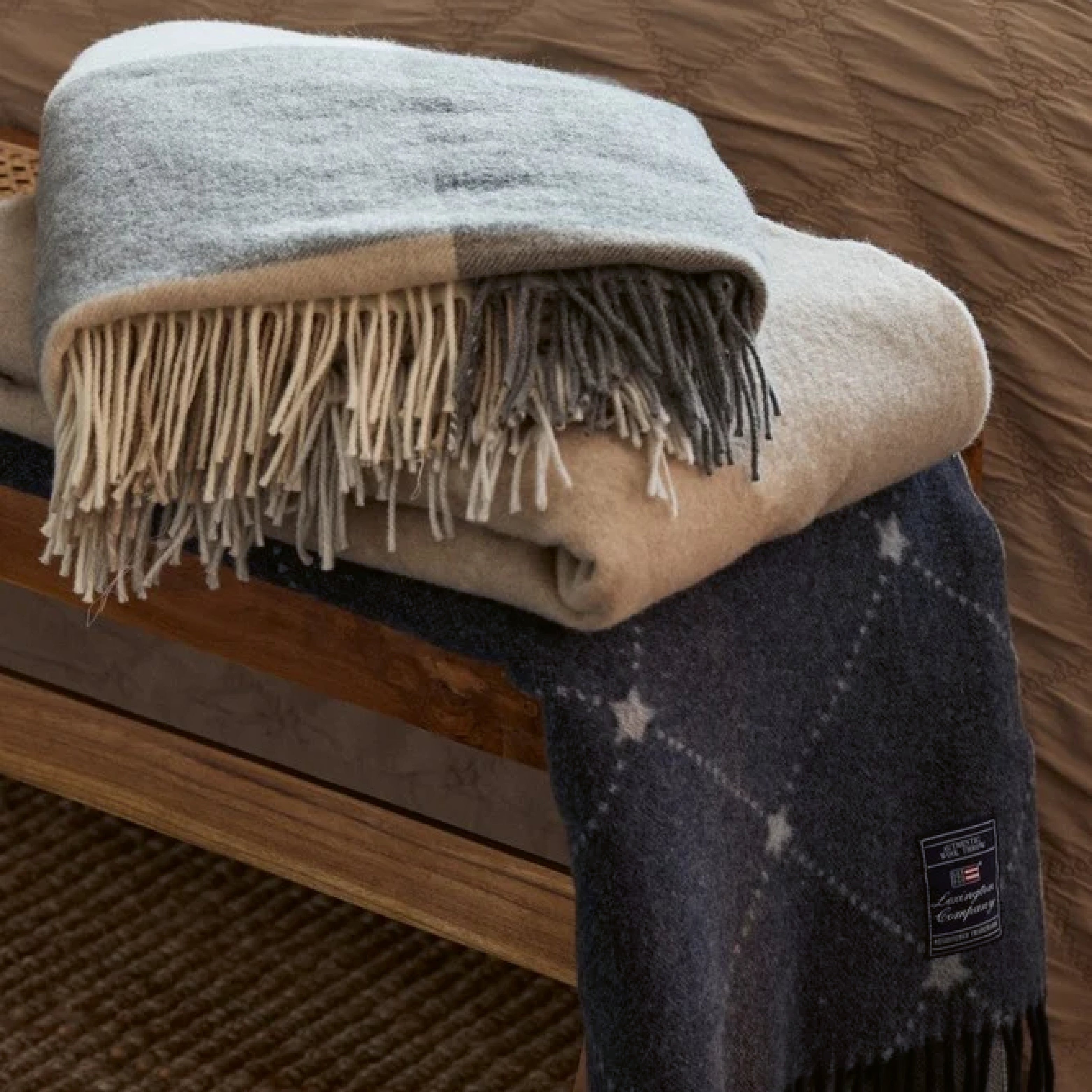 Zwei gefaltete Wolldecken mit Fransen – weiche Plaids aus Naturmaterialien in neutralen Farbtönen, dekorativ über eine Holzbank gelegt