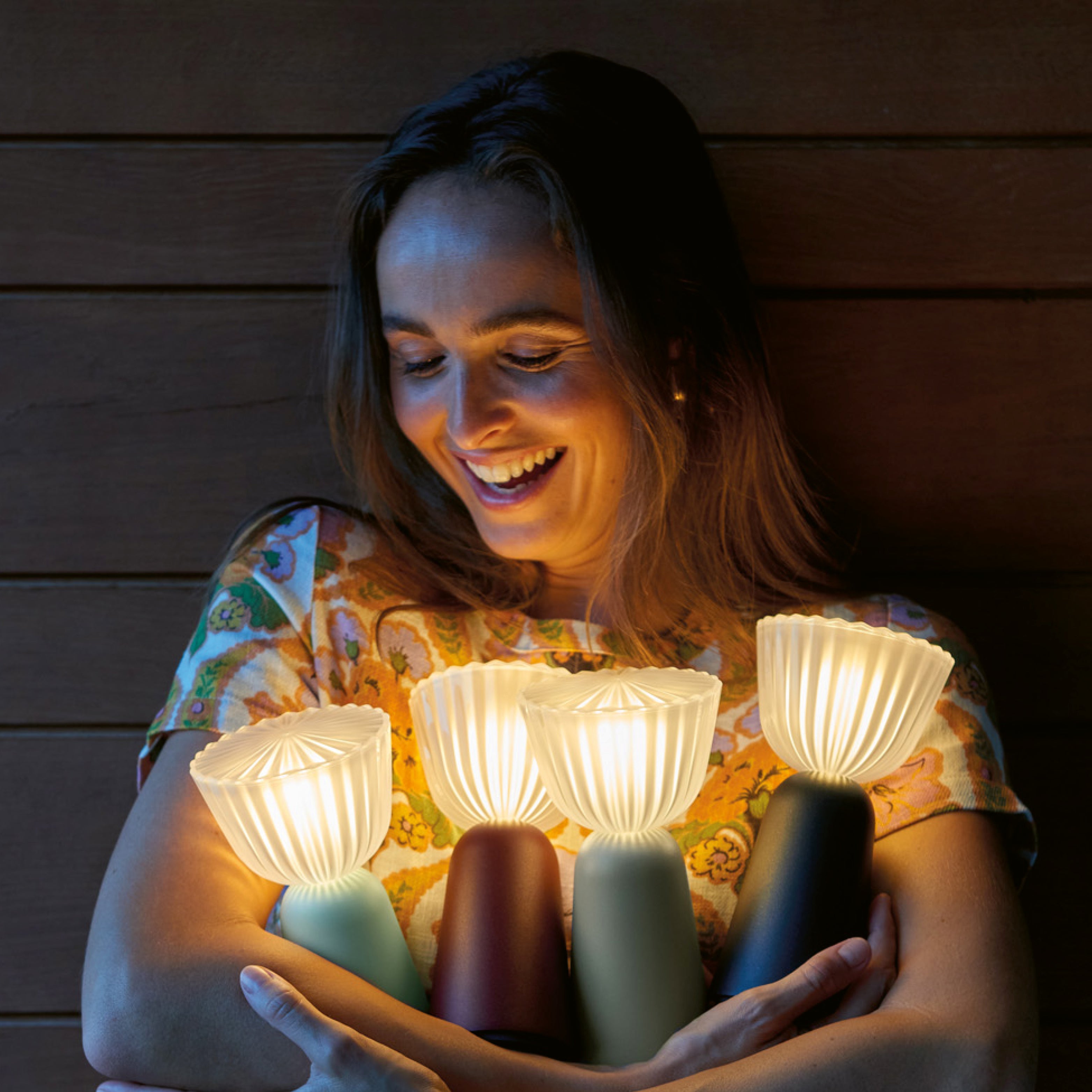 Lächelnde Frau umgeben von mehreren Fermob SWING Außenlampen – stimmungsvolle Outdoor-Beleuchtung mit französischem Designflair