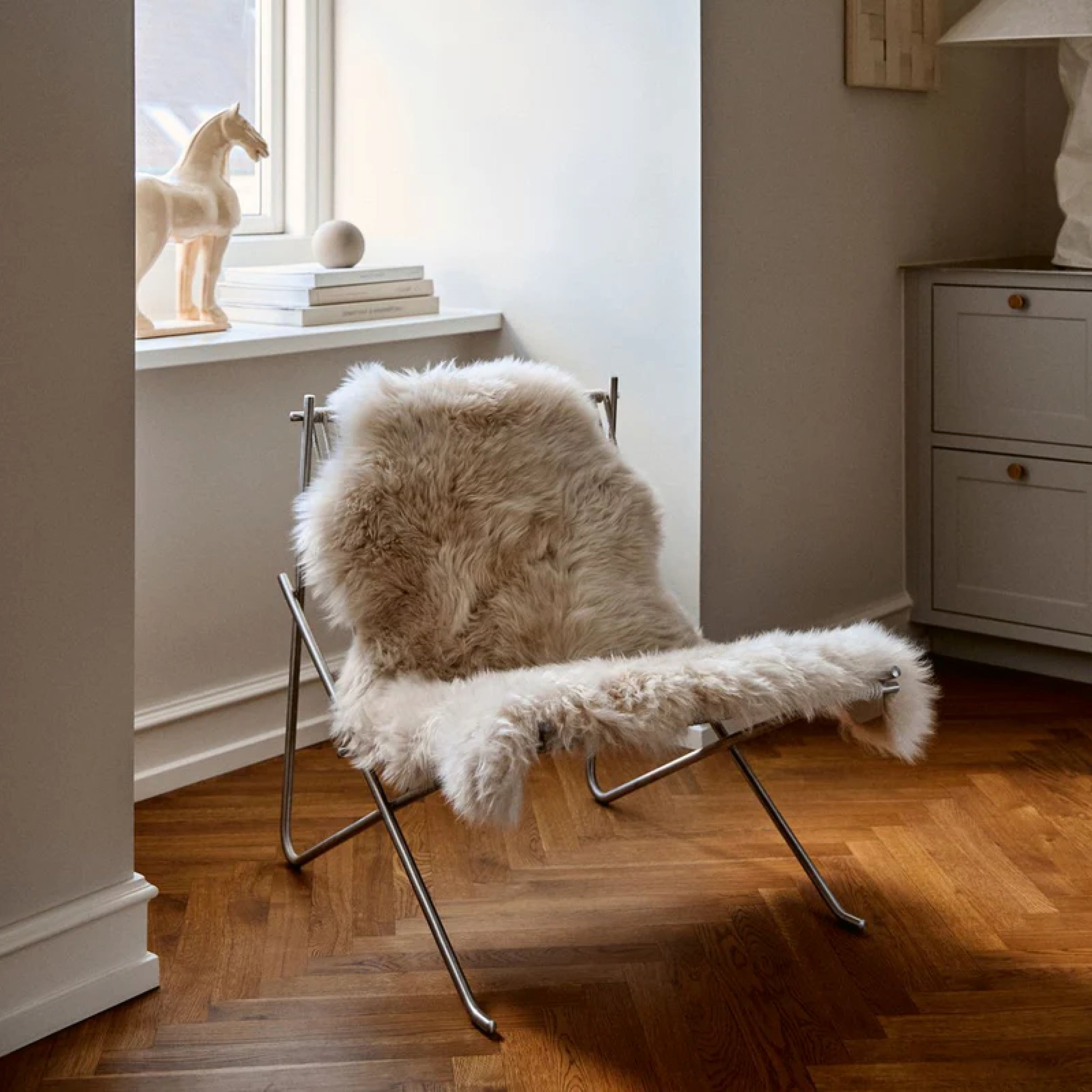 Designsessel mit Lammfellauflage in heller Wohnecke – entspannender Rückzugsort mit natürlicher Wärme und minimalistischer Einrichtung