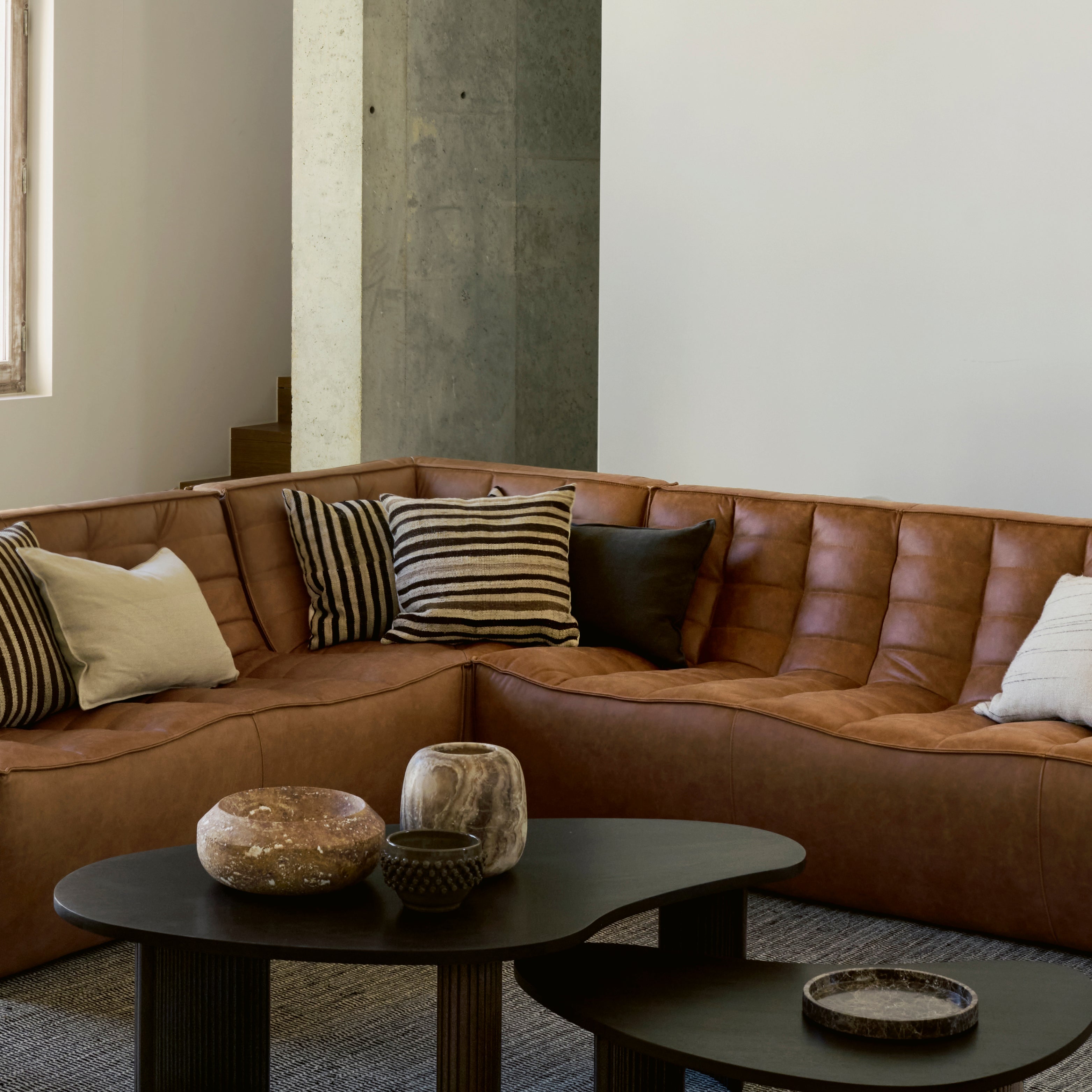 Ethnicraft N701 Sofa aus braunem Leder mit Rautensteppung und Dekokissen – modernes Wohnzimmer mit Couchtisch.