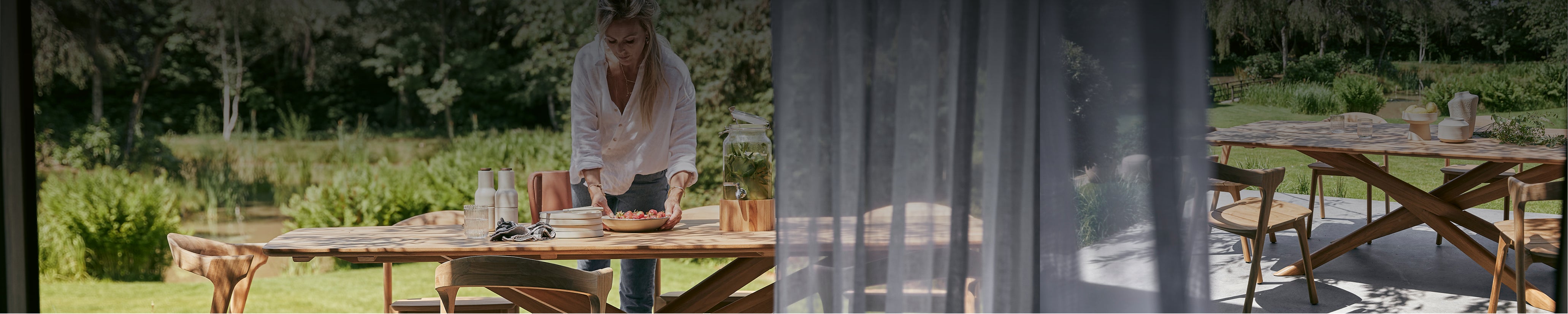 Frau deckt Ethnicraft Gartentisch aus Massivholz – hochwertiges Outdoor-Design in Naturkulisse.