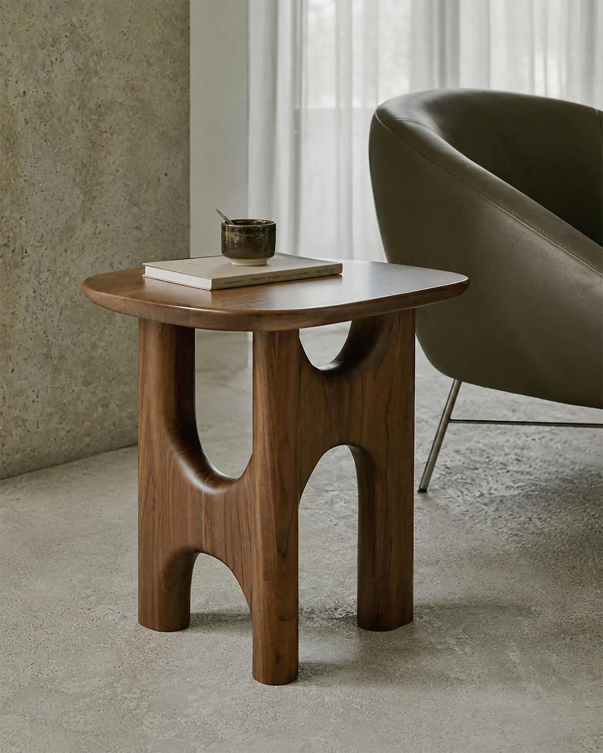 Table d'appoint Ethnicraft FLOW en teck massif, couleur « Wild Brown », servant de support compact à côté d'un fauteuil dans un coin lecture.