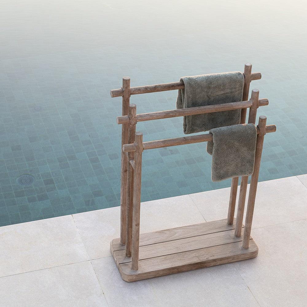 Handtuchträger FINN von Gommaire am Pool platziert – stilvolles Outdoor-Accessoire aus Teakholz, kombiniert mit Liegen und Naturstein